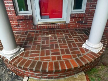 Brick entryway with red door, white columns, and herringbone pattern flooring