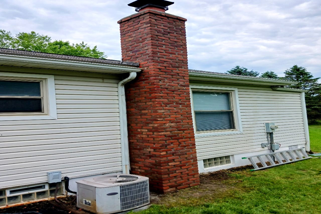 Single-story home with white siding, red brick chimney, garage, and AC unit on grass lawn