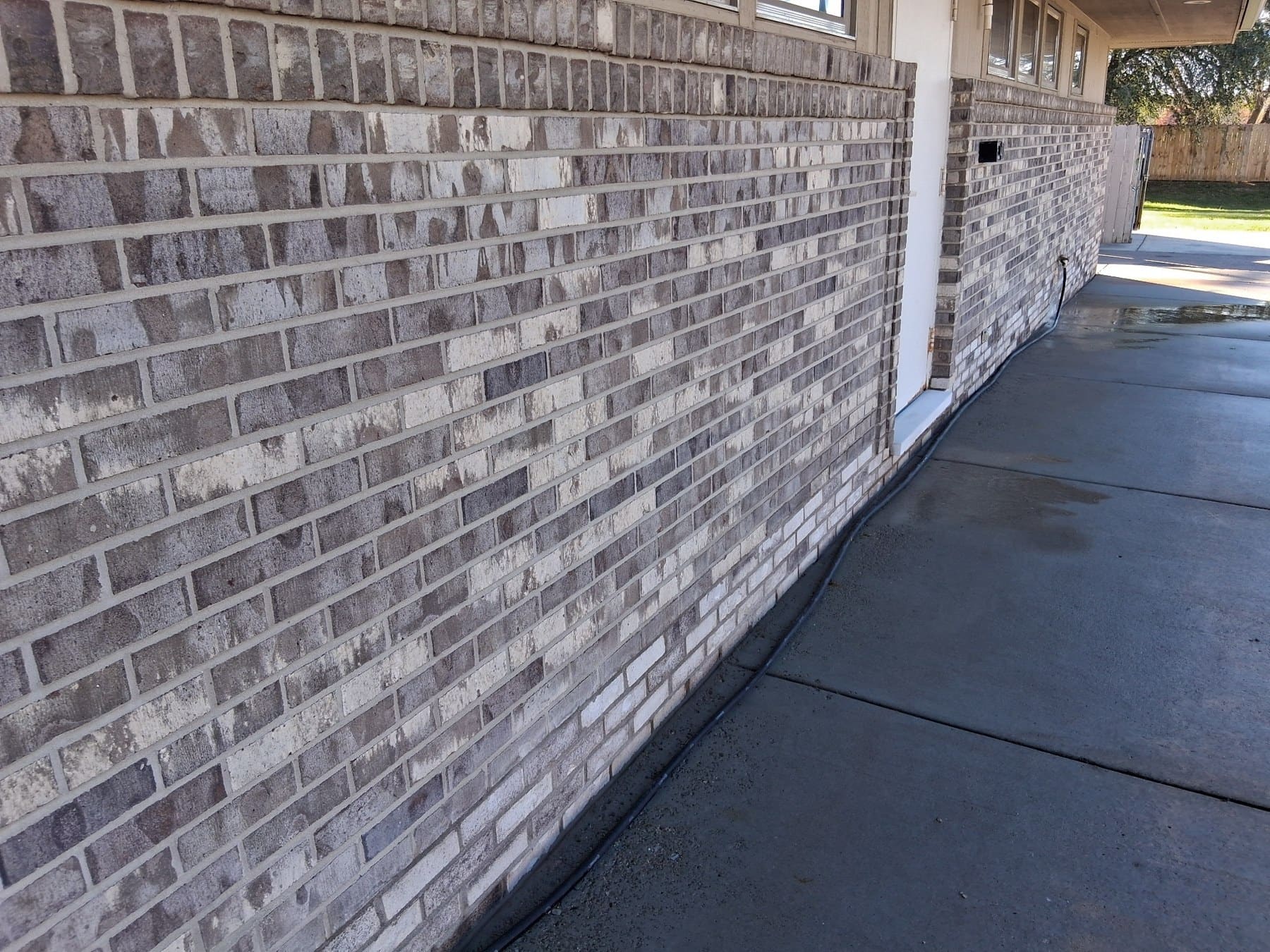 Gray brick exterior wall of residential building with concrete driveway