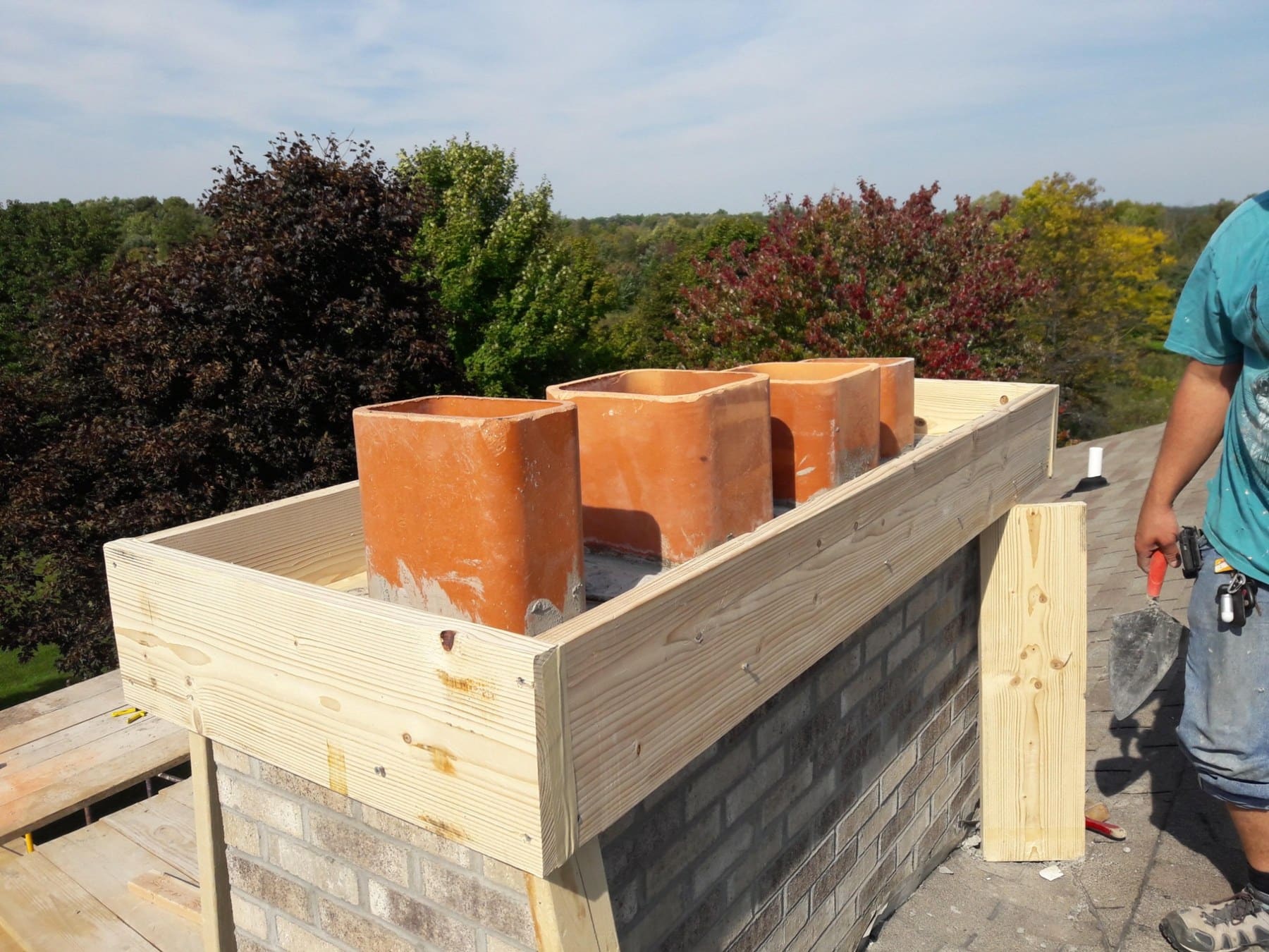 Worker installing copper chimneys on wooden roof structure overlooking forested landscape