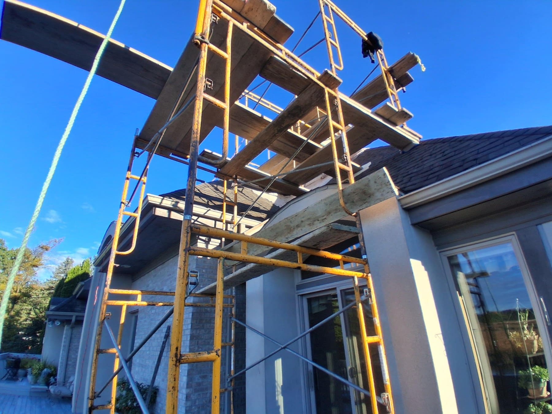 Yellow metal scaffolding erected on modern residential home under construction against clear blue sky