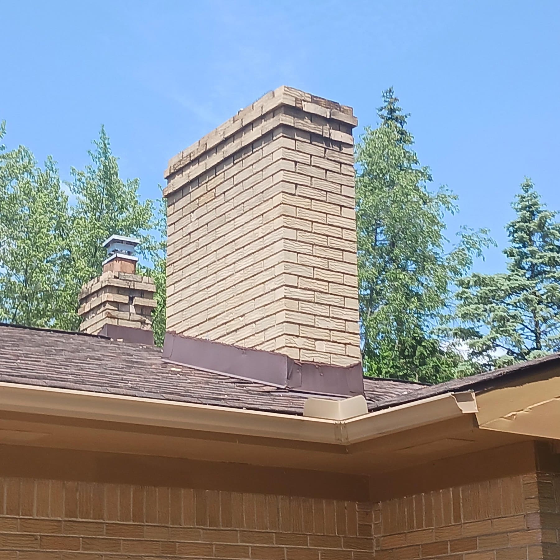 Tall brick chimney rising above residential roofline with surrounding evergreen trees
