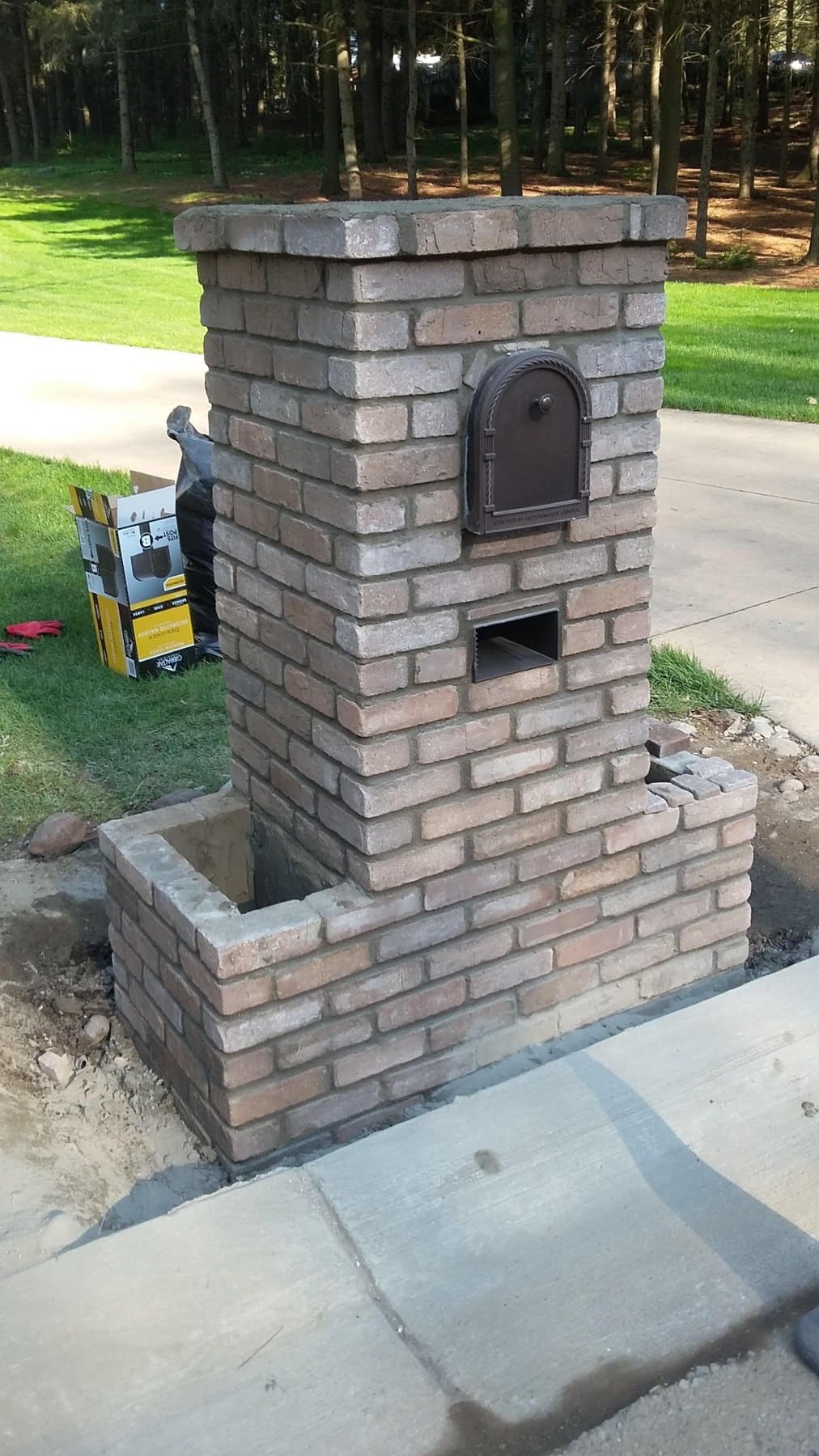 Brick mailbox with black door on residential driveway near lawn