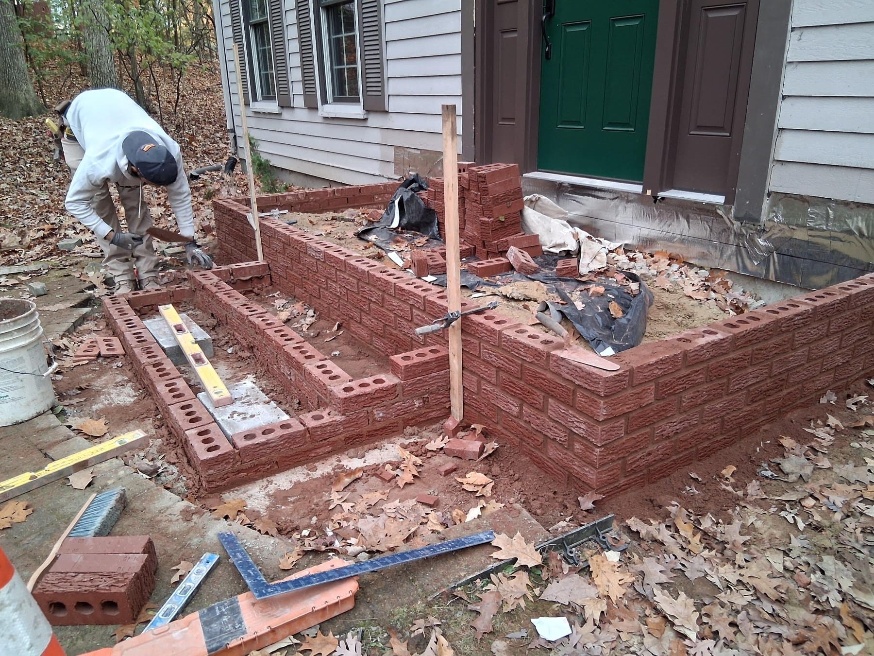 Bricklayer installing red brick foundation and steps beside residential house