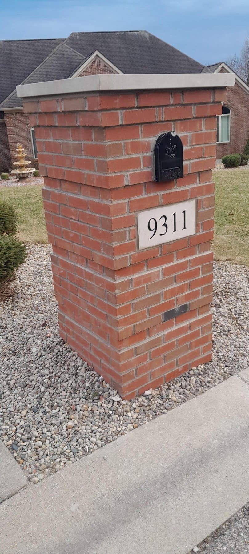 Red brick mailbox post with address 9311 and black mailbox on residential driveway