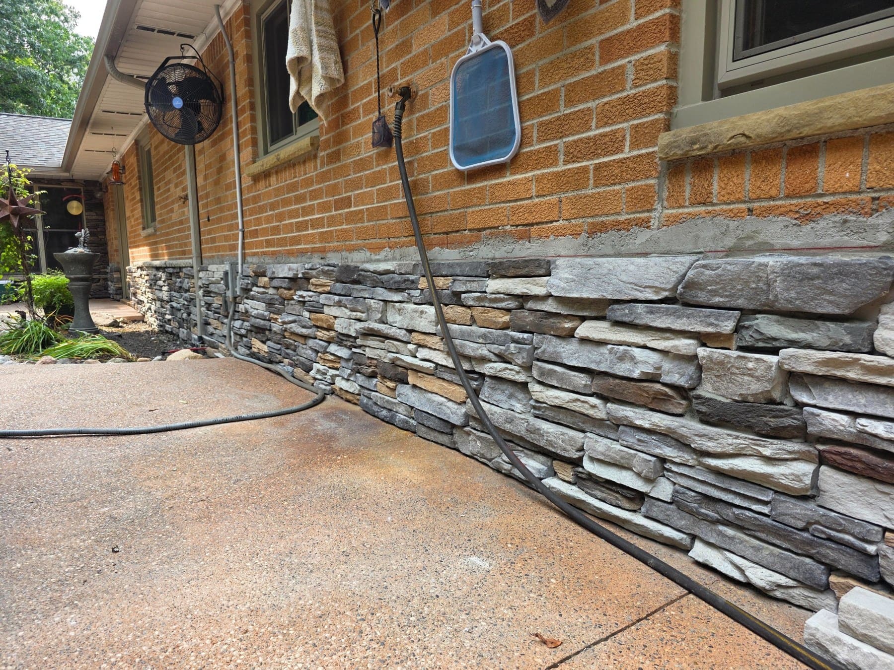 Stone retaining wall along brick house patio with hanging fan and solar light