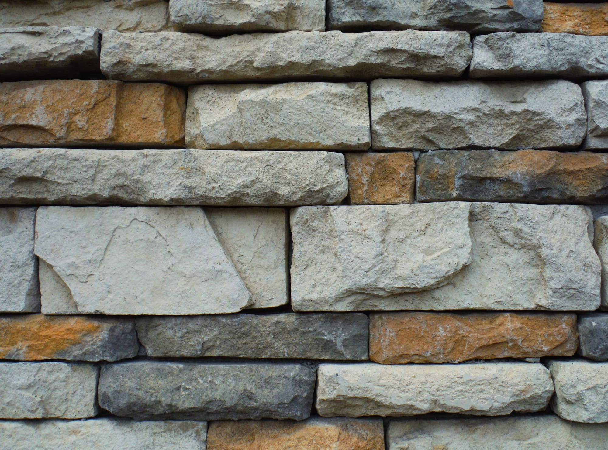 Close-up of stacked stone wall with varied earth-tone rectangular blocks in cream, tan, and gray