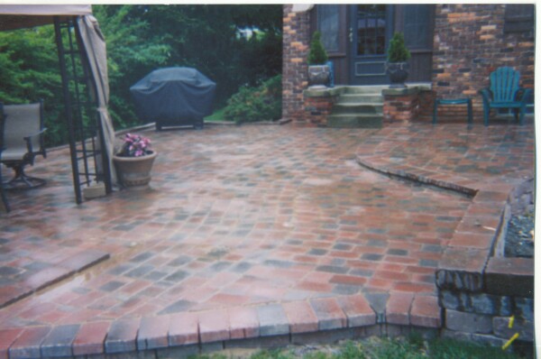 Brick patio with umbrella, outdoor furniture, and brick house with entrance stairs