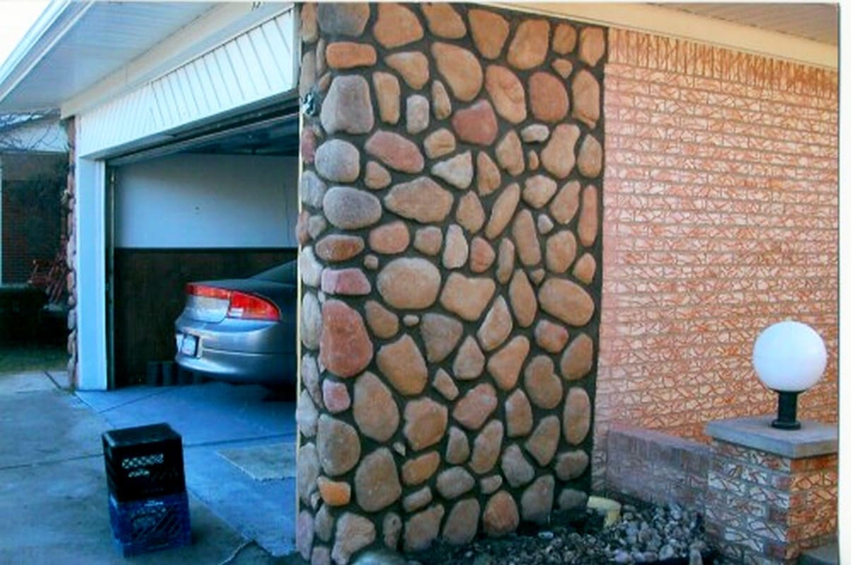 Garage driveway with stone column, brick wall, and parked sedan visible inside