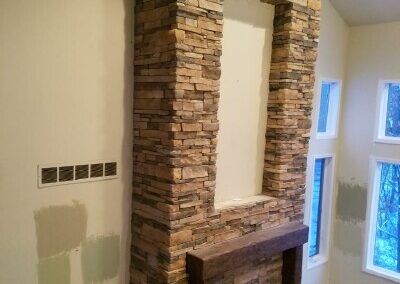 Modern fireplace with stacked stone pillars and wood mantel in contemporary home interior