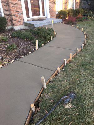Freshly poured concrete walkway with wooden edge forms along residential home foundation