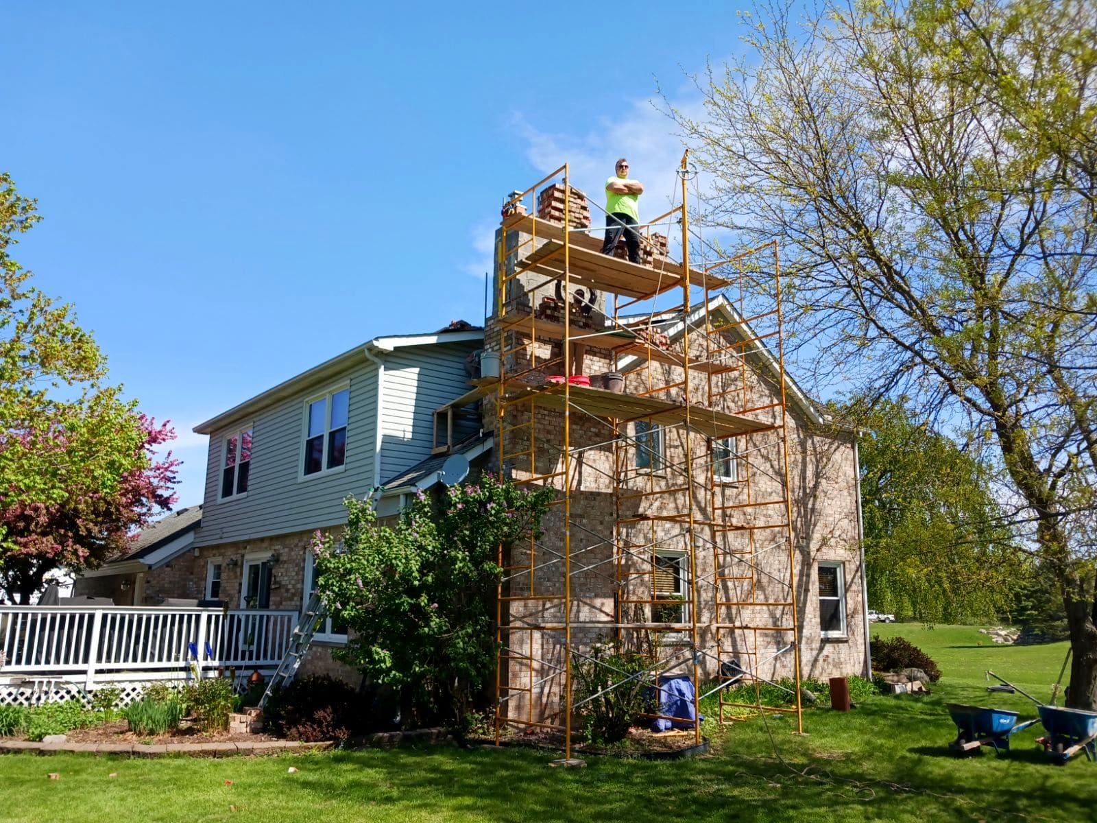Construction worker on scaffolding doing exterior renovation on two-story house with stone and siding